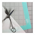 Quilters Select silicone mat in use under fabric and shears, with a gridded ruler alongside